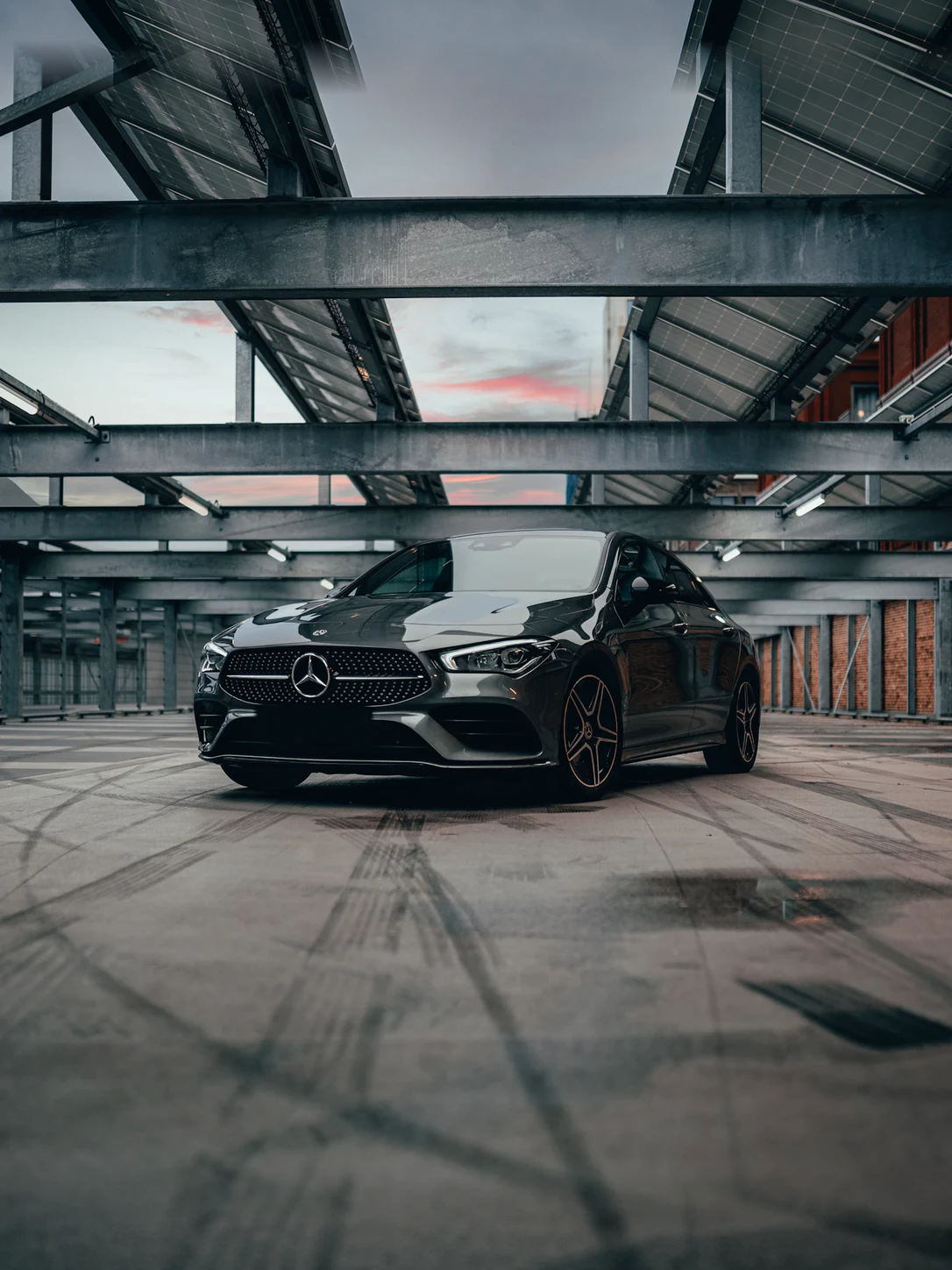 Dark executive sedan parked under a covered deck at dusk
